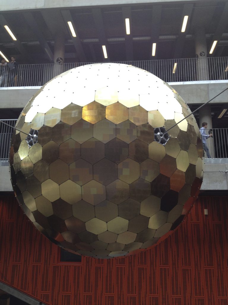A globe made up of hexagonal gilded glass panels, suspended from the ceiling.